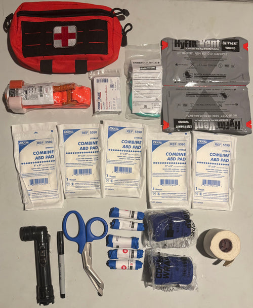 Kit includes pouch with a white cross, tourniquet, Mylar blanket,  Nasopharyngeal airway, pair of vented chest seals, 5- 5 x 9 dressings, flashlight, permanent marker, trauma shears, 5 pairs of nitrile gloves, 2 rolls self adhering bandages, 1 roll 2 inch cloth tape